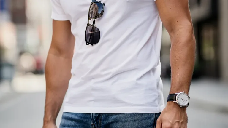 Stylish person wearing minimalist watch, silver necklace, and sunglasses with t-shirt and jeans