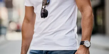 Stylish person wearing minimalist watch, silver necklace, and sunglasses with t-shirt and jeans