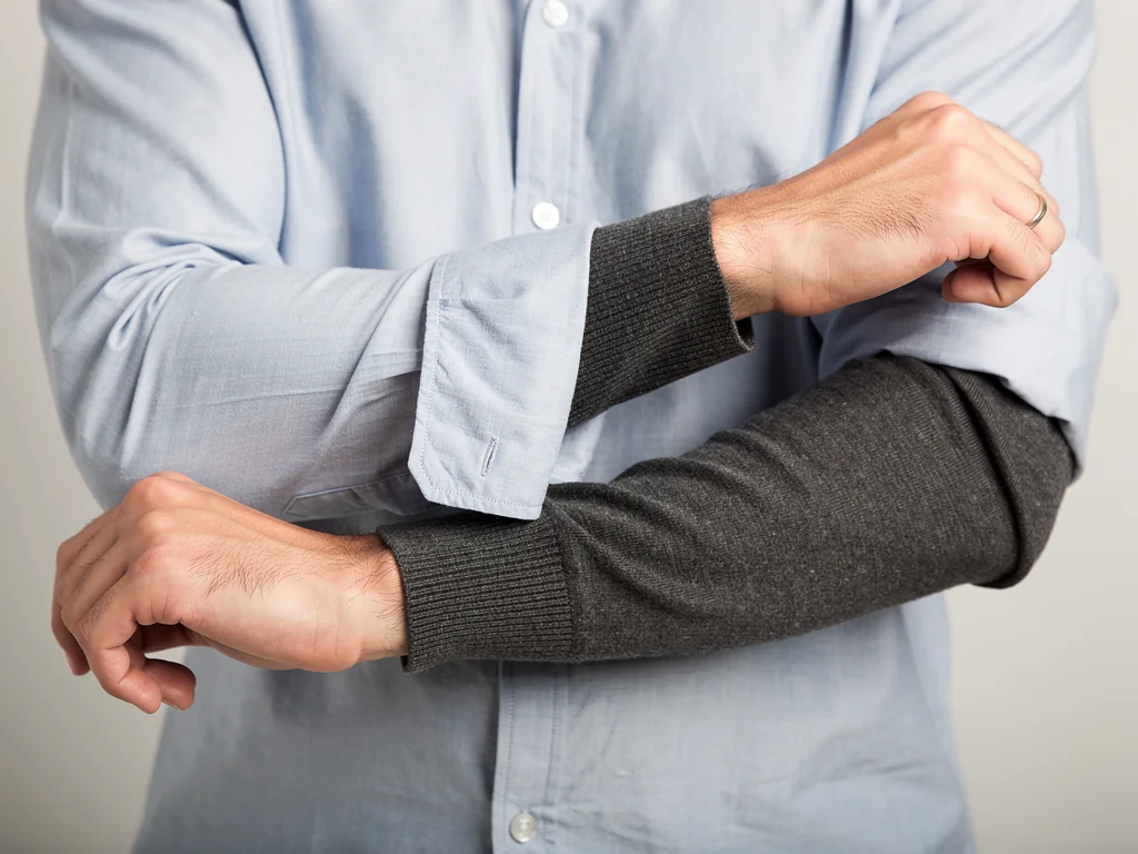Person adjusting sleeves of a layered outfit, showing contrasting textures